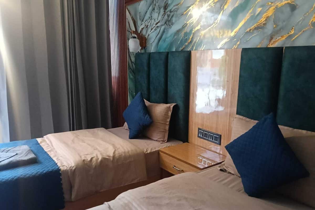 A hotel room with two beds, a wooden nightstand, a marble wall, and a window with curtains.