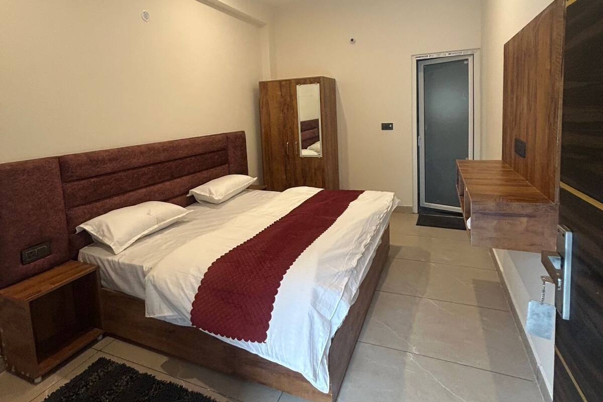 A bedroom with a bed, a ceiling fan, a wooden wardrobe, a mirror, and a door.