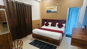A bedroom with a bed, a chair, a ceiling fan, and a wooden wall panel. - La Casa Bonita (Rishikesh)
