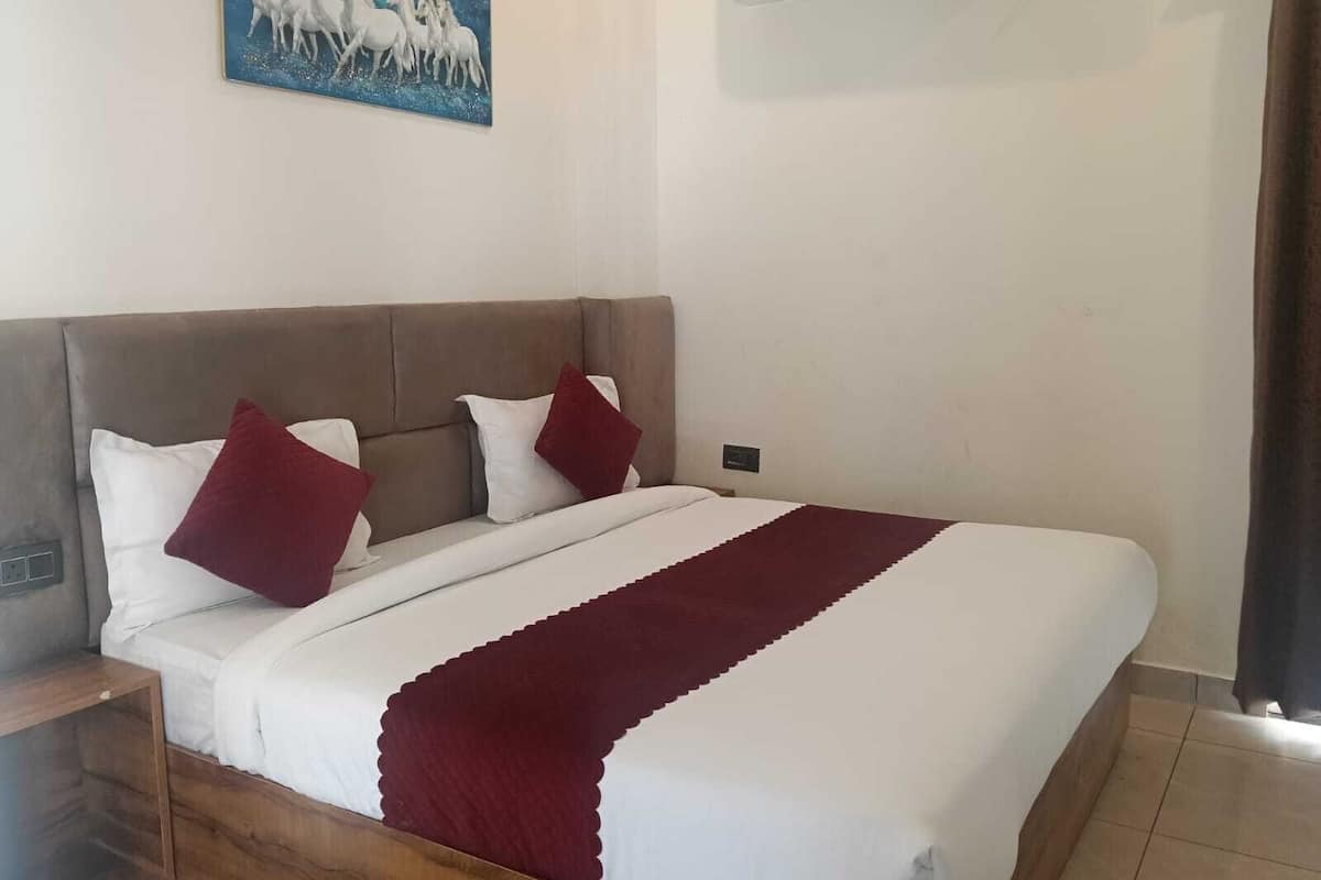 A bedroom with a large bed, two pillows, a red throw blanket, and a painting of horses on the wall.