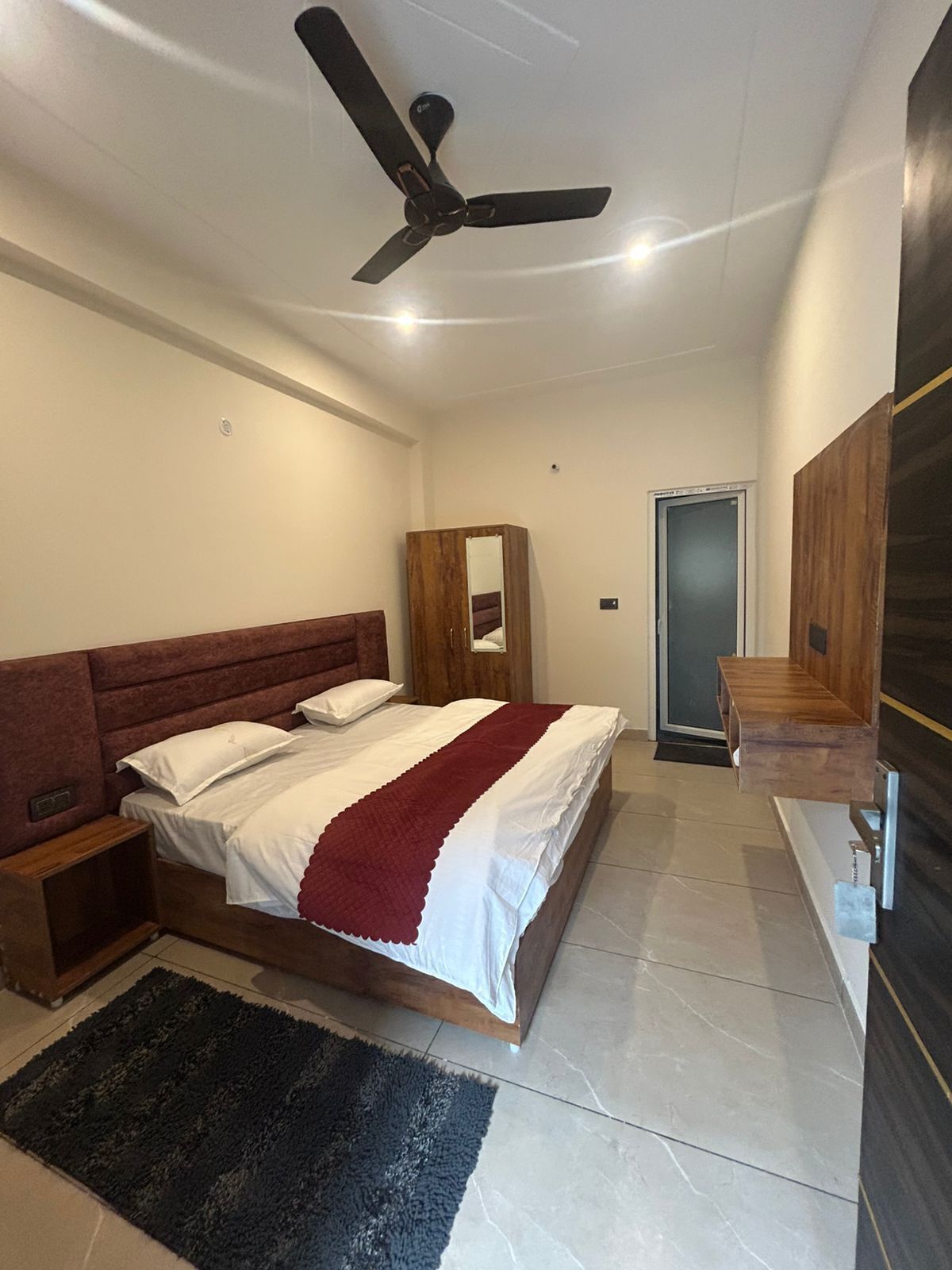 Un dormitorio con una cama, ventilador de techo, armario de madera, espejo y una puerta.