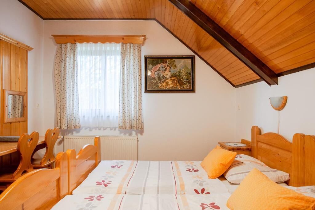 A bedroom with a wooden ceiling, a bed with floral bedding, a window with curtains, and a framed picture on the wall.