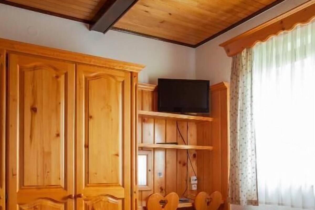 Un dormitorio de madera con una cama, un televisor en un estante y una ventana con cortinas.