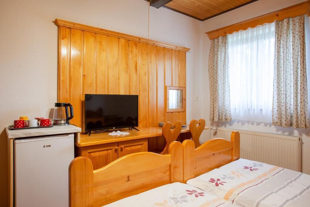 A cozy room with a wooden bed, a TV, a small fridge, and a window with curtains.
