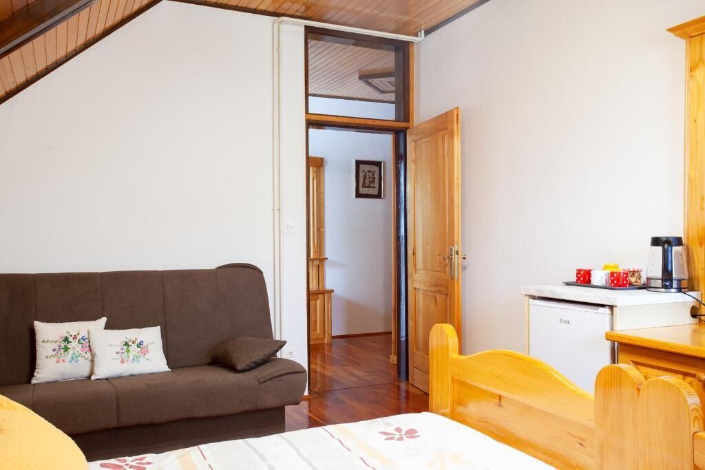 Ein gemütliches Zimmer mit braunem Sofa, einem Holzstuhl, einem kleinen Schreibtisch mit Kaffeemaschine und einem weißen Kühlschrank.