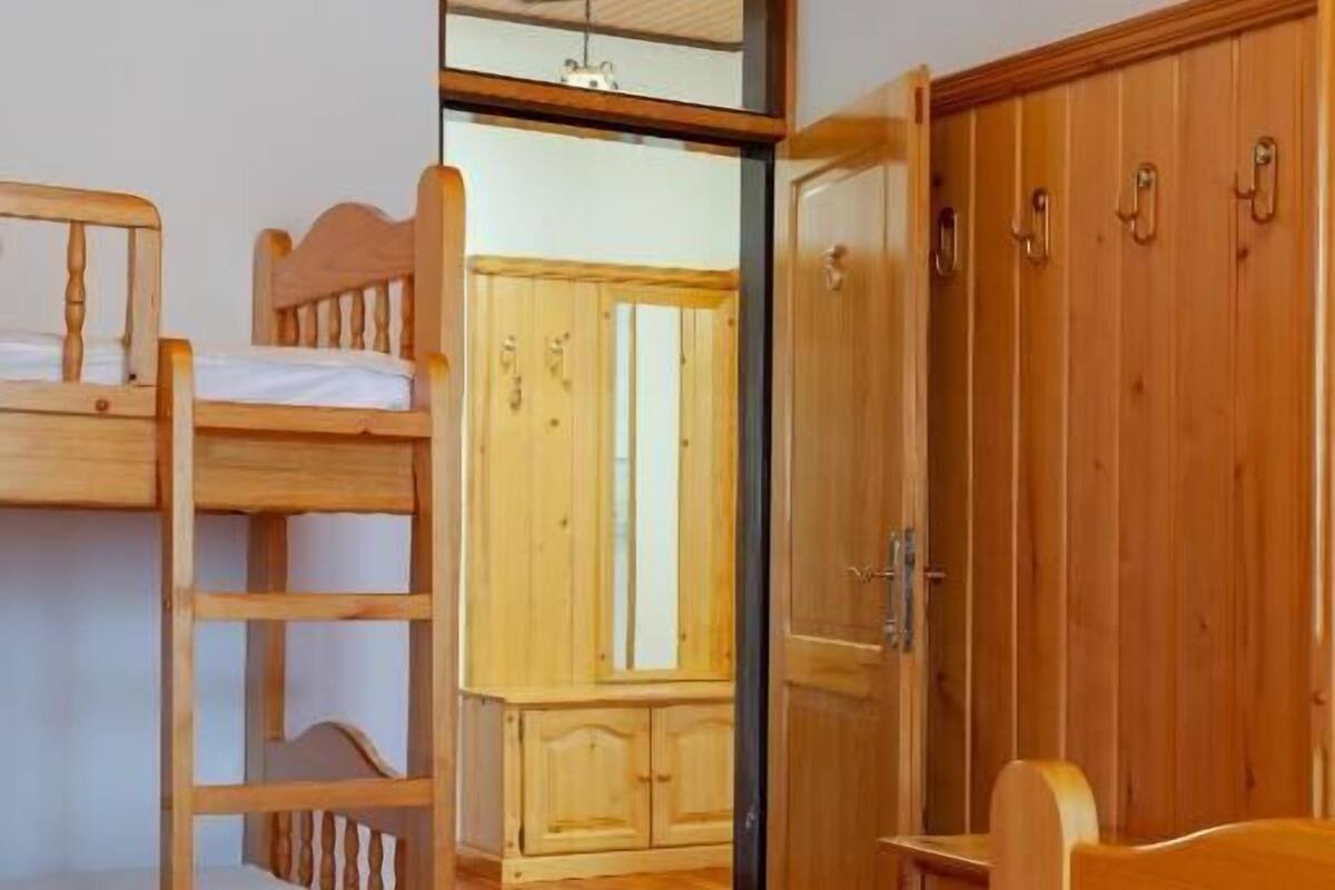 Una habitación con una cama litera, un armario de madera y una puerta que da a otra habitación.