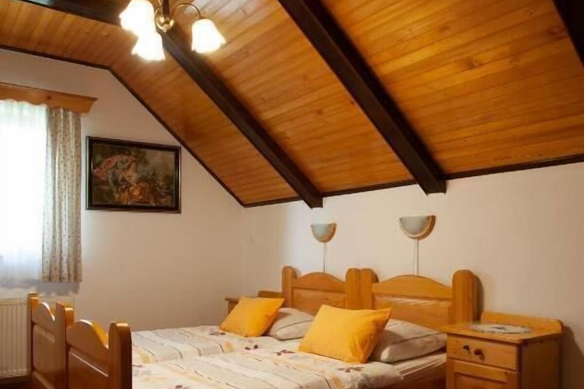 Un dormitorio con techo inclinado, estructura de cama de madera, dos mesitas de noche y una ventana con cortinas.