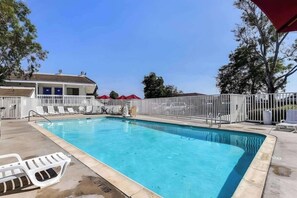 A swimming pool with a white fence, lounge chairs, and a building with a blue door in the background. - Super 8 by Wyndham Livermore (Livermore)