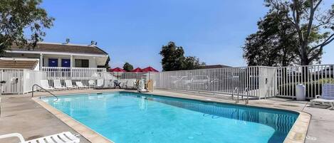 A swimming pool with a white fence, lounge chairs, and a building with a blue door in the background.
