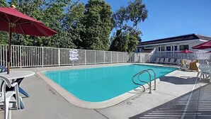 Une piscine entourée d’une clôture blanche, avec des chaises longues et des parasols.