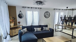 A modern living room with a sectional sofa, a wooden coffee table, and a dining area with chairs and a table. - Large apartment between Paris - Disneyland - CDG Airport - B.Olympique Vaires (Brou-sur-Chantereine)