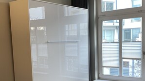A modern room with a large white cabinet, a dining table with chairs, and a window with blinds.
