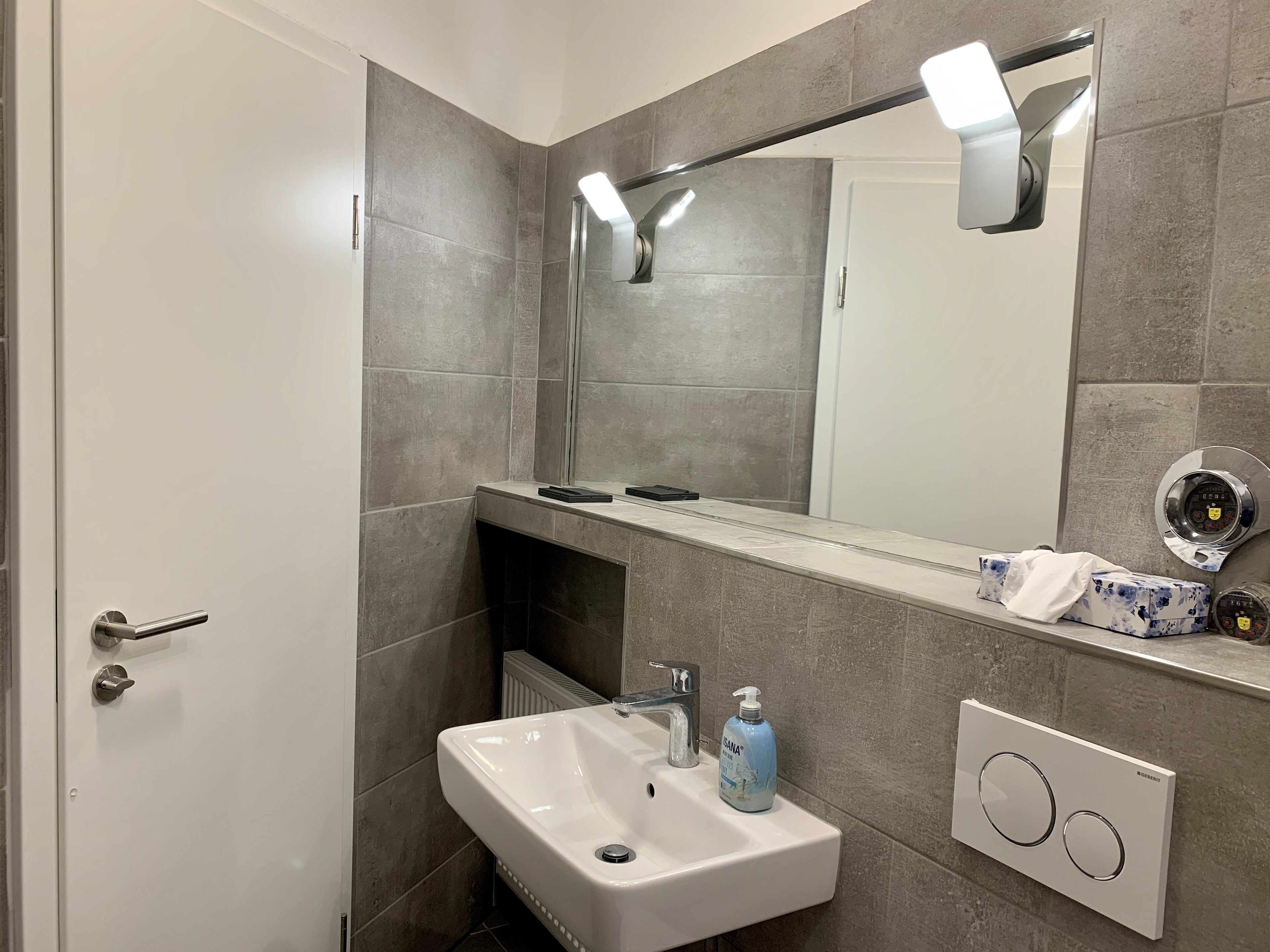 Une salle de bain moderne avec un lavabo blanc, un miroir, un distributeur de serviettes et un sèche-mains.