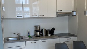 A modern kitchen with white cabinets, a stainless steel sink, a coffee maker, and a dining table with chairs.