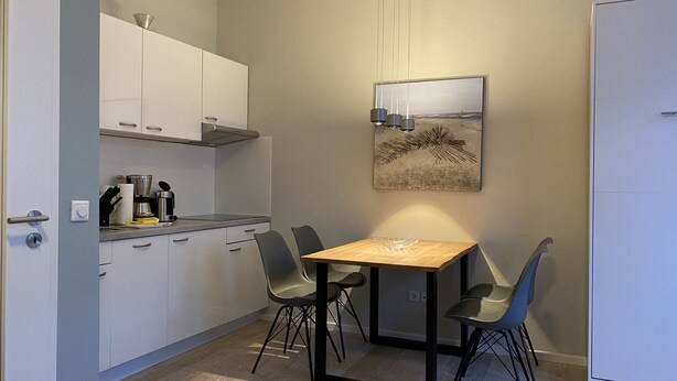 A compact kitchen with white cabinets, a coffee maker, and a table with two chairs.