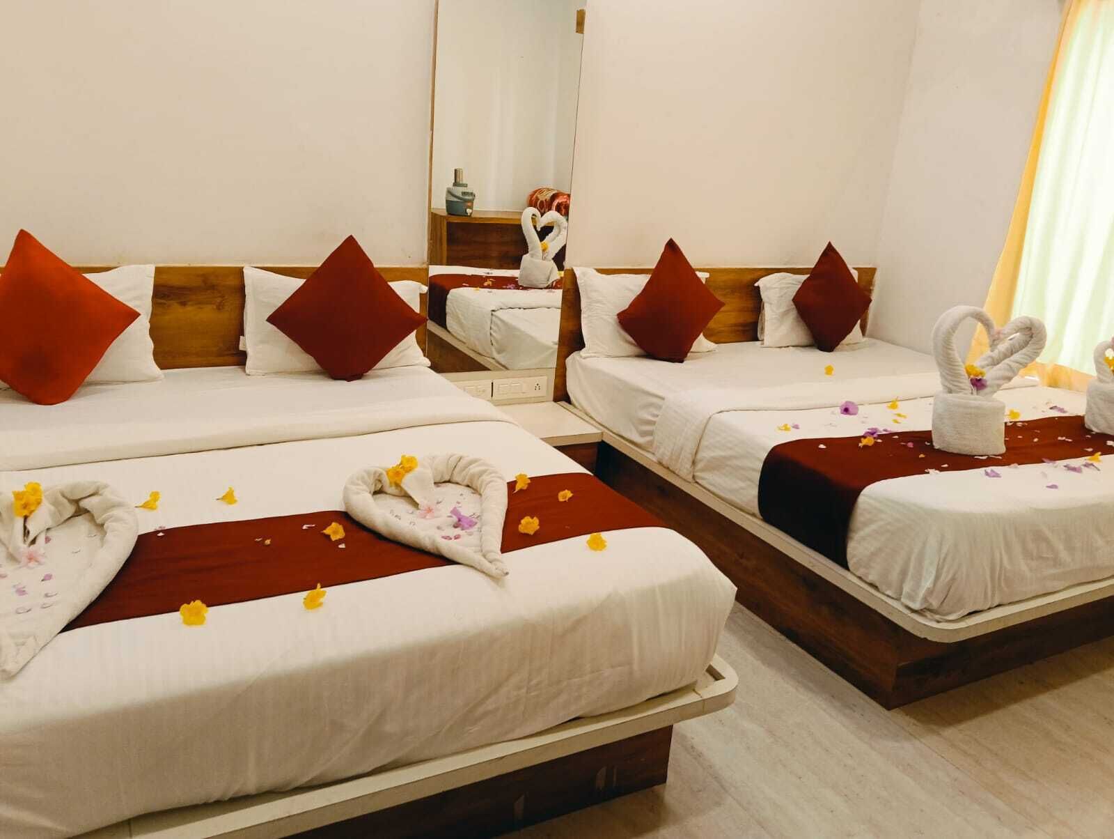 A hotel room with two beds, each with white linens, red pillows, and a brown throw blanket. There are decorative swans and flower petals on the beds.