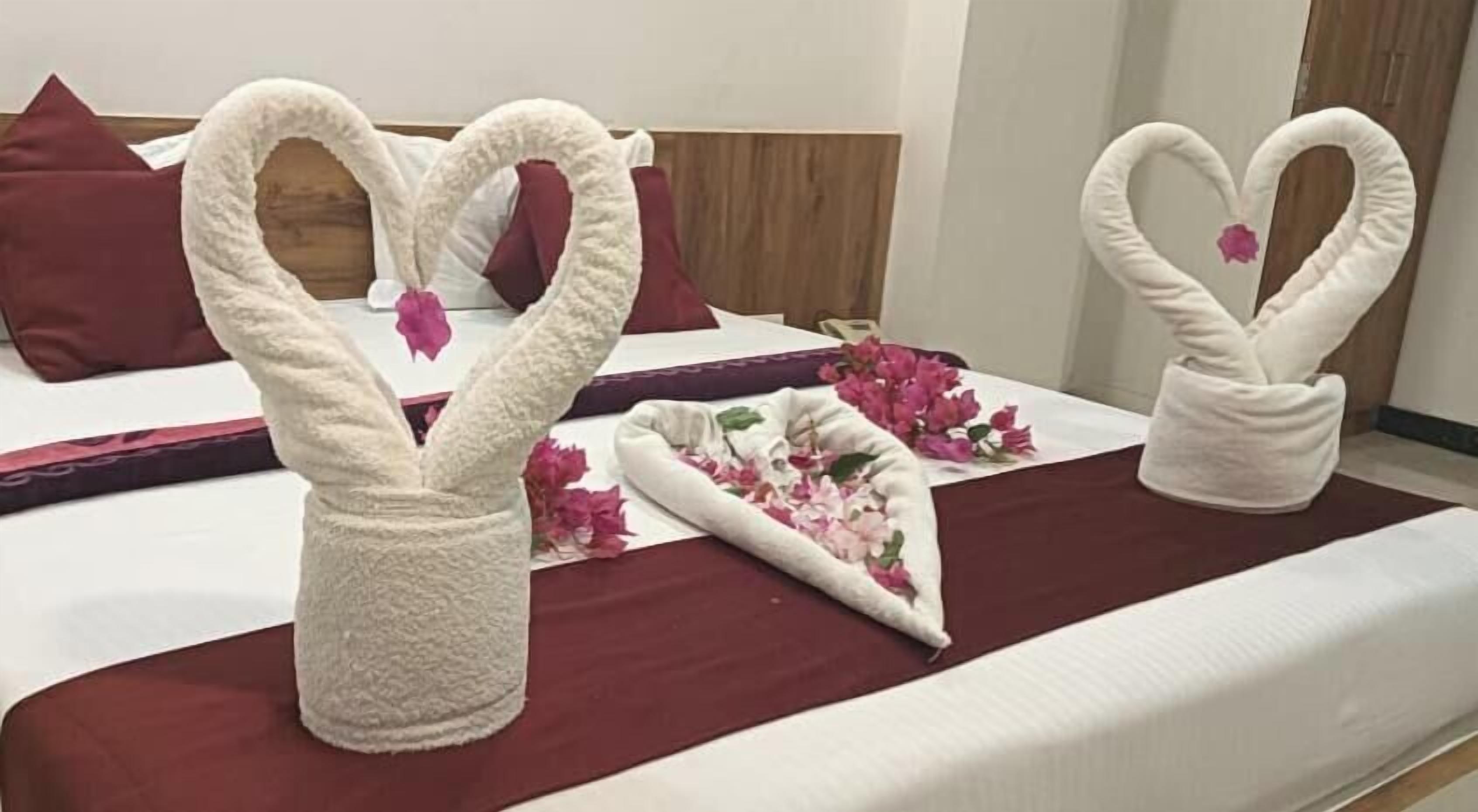 Habitación de hotel con una cama, almohadas y una decoración de toallas con forma de cisnes y flores.