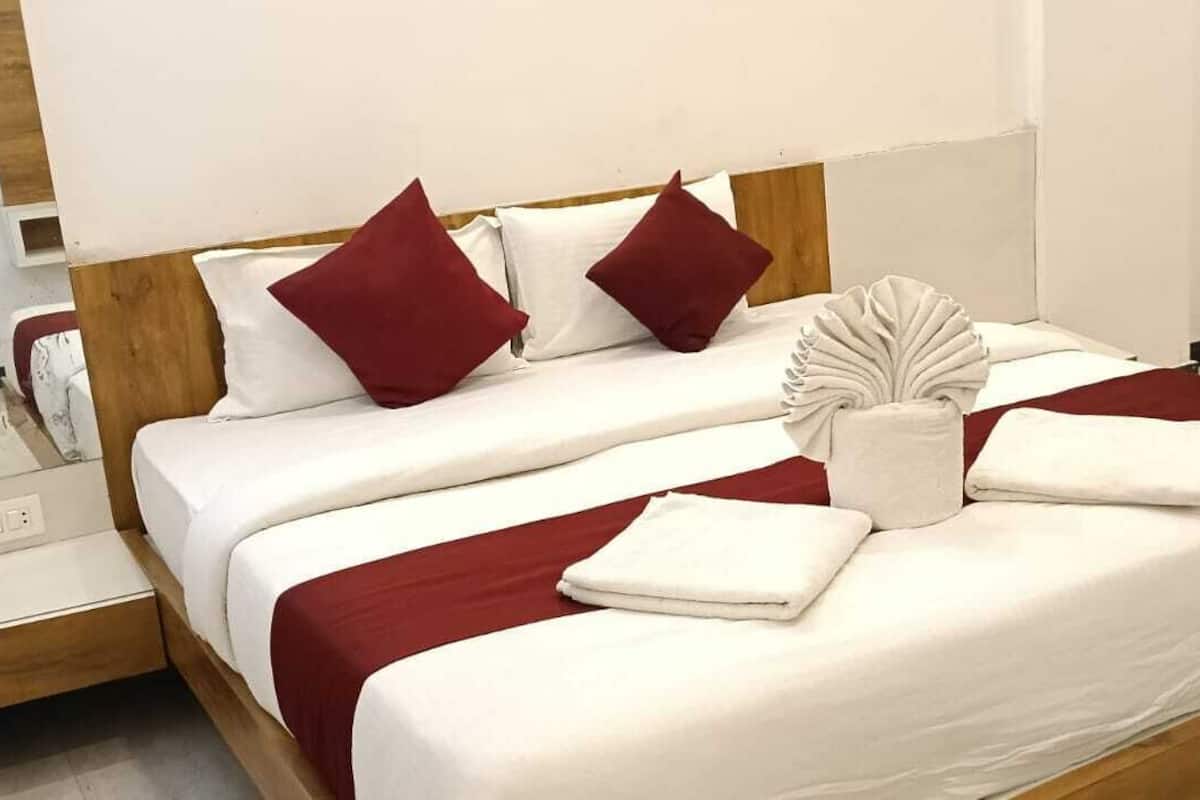 A neatly made bed with white linens, red pillows, and a decorative vase.