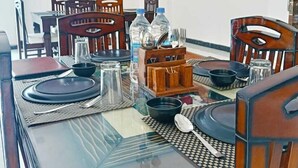 A dining area with a glass-top table, wooden chairs, and a buffet stand with water bottles and utensils. - Leopard Valley Resort (Kumbhalgarh)