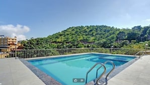 A rectangular pool with metal railings, surrounded by a fence, with a mountainous landscape in the background. - Leopard Valley Resort (Kumbhalgarh)