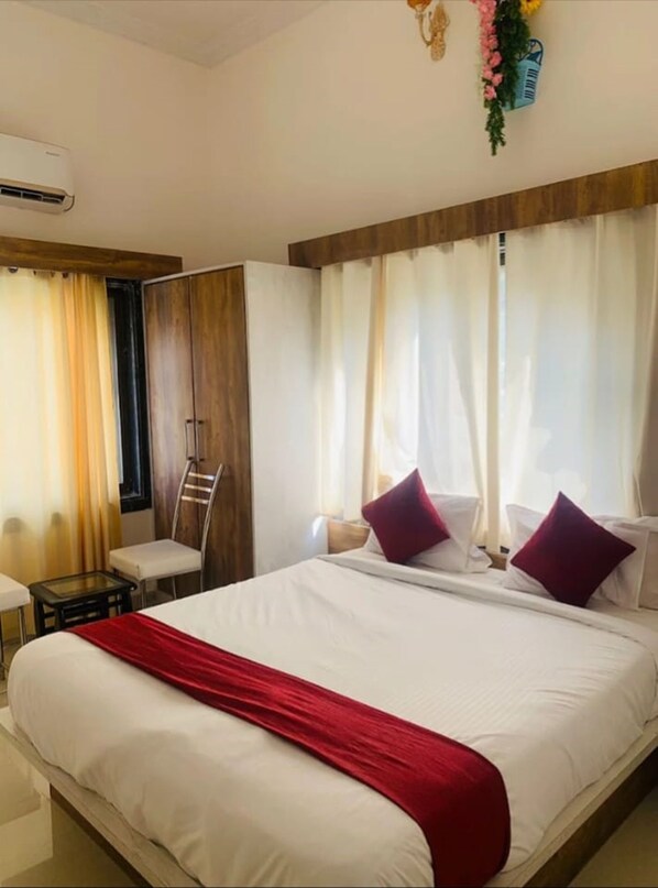 A hotel room with a large bed, a desk, a chair, and a window with curtains.