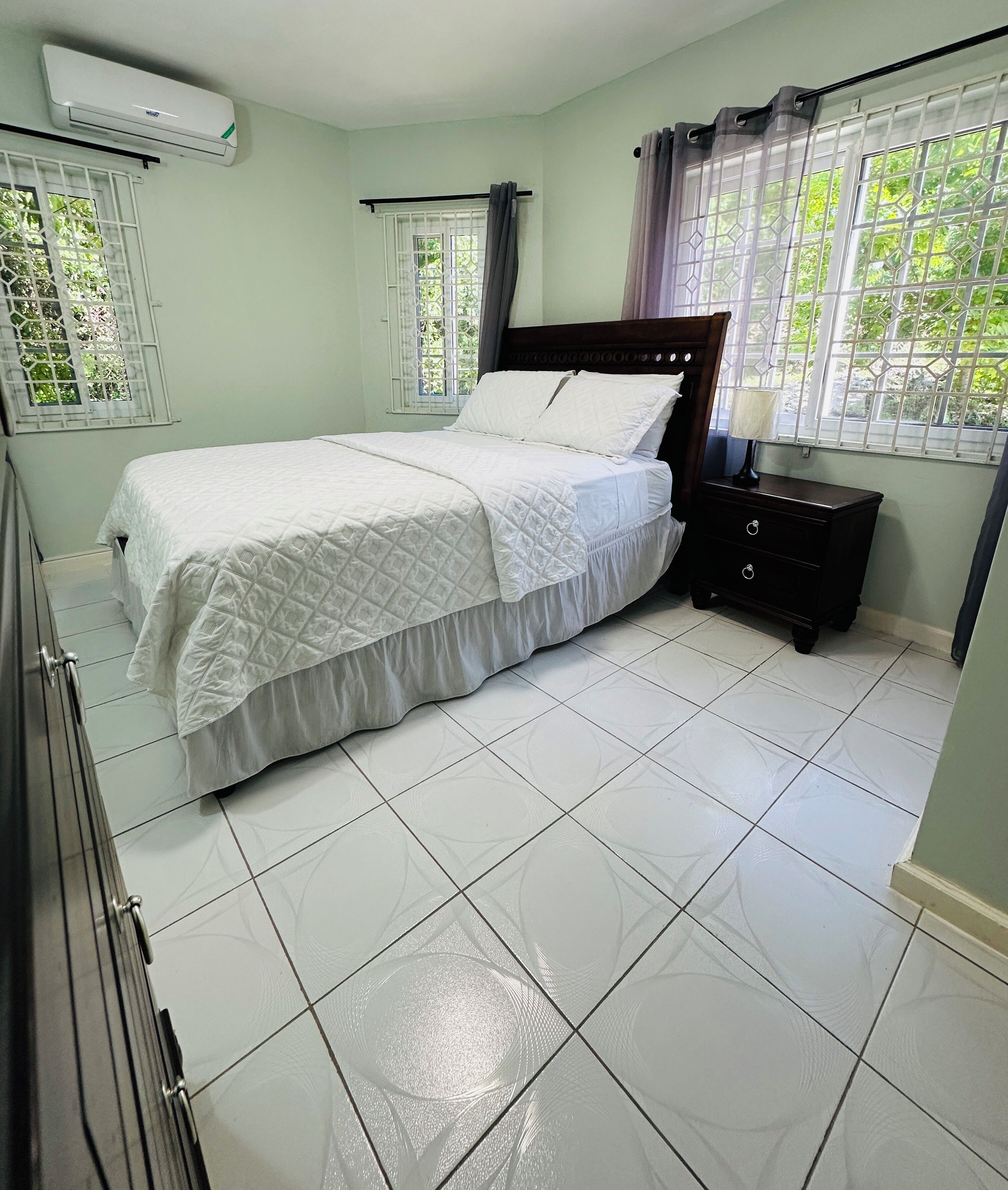 A bedroom with a bed, a dresser, a nightstand, and a window with curtains.