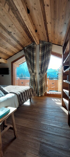 A room with a wooden ceiling, a bed with a striped blanket, a wooden floor, and a view of a wooden deck and mountains through a window. - L'Échappée Chalet sauna 7 bdrms terraces sublime view skiroom close to cable car (Champagny-en-Vanoise)