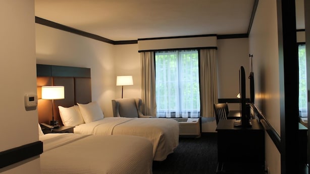 A hotel room with two beds, a desk, a chair, a TV, and a window with curtains.