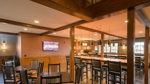 A restaurant with wooden tables and chairs, a bar area, and a television mounted on the wall.