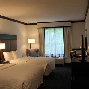 A hotel room with two beds, a desk, a chair, a lamp, and a window with curtains. - Craftsman Inn and Conference Center (Fayetteville)