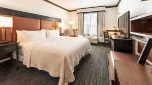 A hotel room with a large bed, bedside tables, a desk, a chair, a TV, and a window with curtains. - Craftsman Inn and Conference Center (Fayetteville)