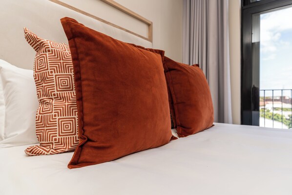 A bed with two large pillows, one patterned and one solid orange, in a room with a view of a balcony. - Harbourline Haven | Signature #304 | De Waterkant (Cape Town)