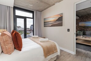 Ein modernes Hotelzimmer mit einem großen Bett, Blick auf die Stadt durch ein großes Fenster und einem Gemälde an der Wand.