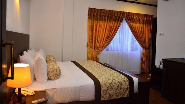 A hotel room with a bed, a desk, a lamp, and a window with curtains. - Hotel Jojos (Nuwara Eliya)