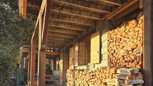 A wooden building with a covered porch, a stone wall, and a stack of firewood. - 37 m2 apartment in RDC chalet with south-facing lake view (Puy-Sanières)