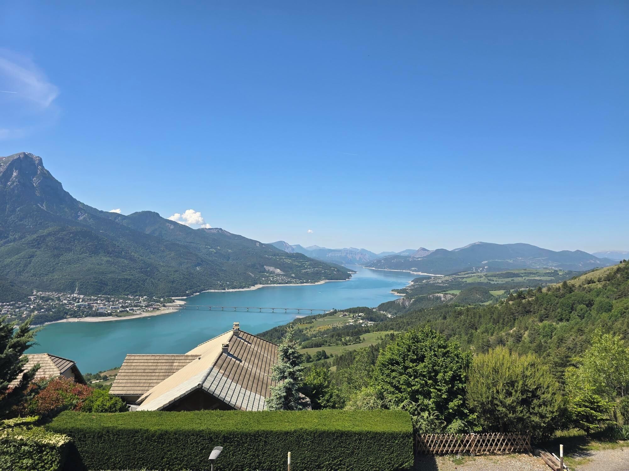 Un paysage montagneux avec un lac, un pont et un bâtiment doté d’un toit en pente.