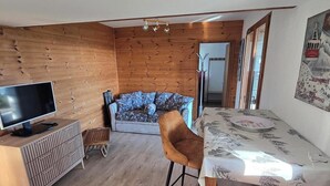 A modern living room with a wooden wall, a sofa, a TV, and a dining area with a table and chairs. - 37 m2 apartment in RDC chalet with south-facing lake view (Puy-Sanières)
