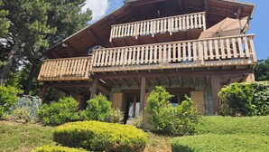 A two-story wooden chalet with a balcony, surrounded by well-maintained hedges and trees. - 37 m2 apartment in RDC chalet with south-facing lake view (Puy-Sanières)