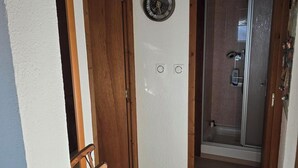 Ein Flur mit Holzboden, einem Holzstuhl, einer Wanduhr und einer Tür zu einem Badezimmer mit Dusche.