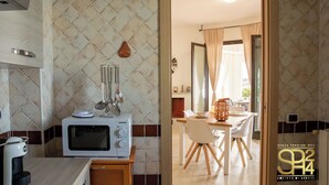 A kitchen with a microwave, a coffee machine, and a blender on a counter. There is a dining area with a table and chairs visible through an open doorway. - Villa Stone and Sea (Villa Almar) (Alghero)