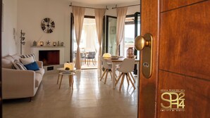 A modern living room with a sofa, a fireplace, a dining area with a table and chairs, and a large window with curtains. - Villa Stone and Sea (Villa Almar) (Alghero)