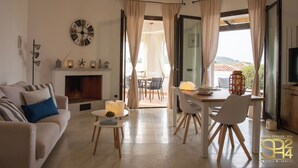 A modern living room with a fireplace, a dining area, and a view of the outdoors. - Villa Stone and Sea (Villa Almar) (Alghero)