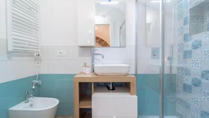 A modern bathroom with a white sink, a mirror above it, a shower with patterned tiles, and a toilet. - Domo Masial - Alghero (Alghero)