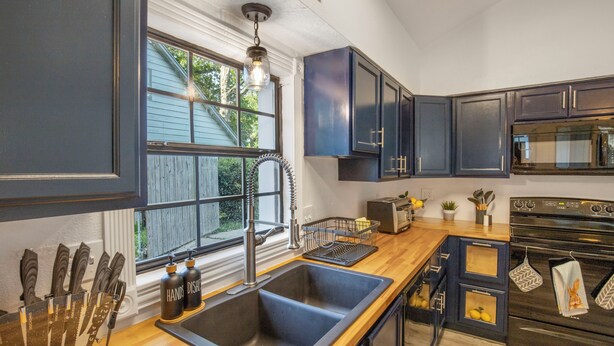 A modern kitchen with dark cabinets, a wooden countertop, a stainless steel sink, and a built-in oven.