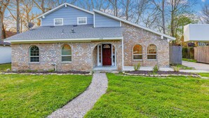 A two-story brick house with a red door, a gravel driveway, and a well-maintained lawn.