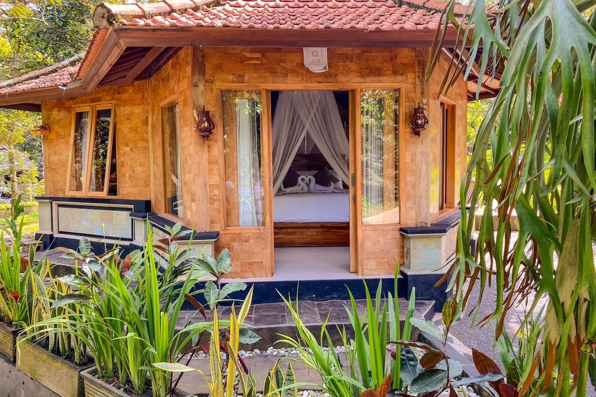 A wooden cabin with a tiled roof, a bed with a canopy, and a garden with various plants.