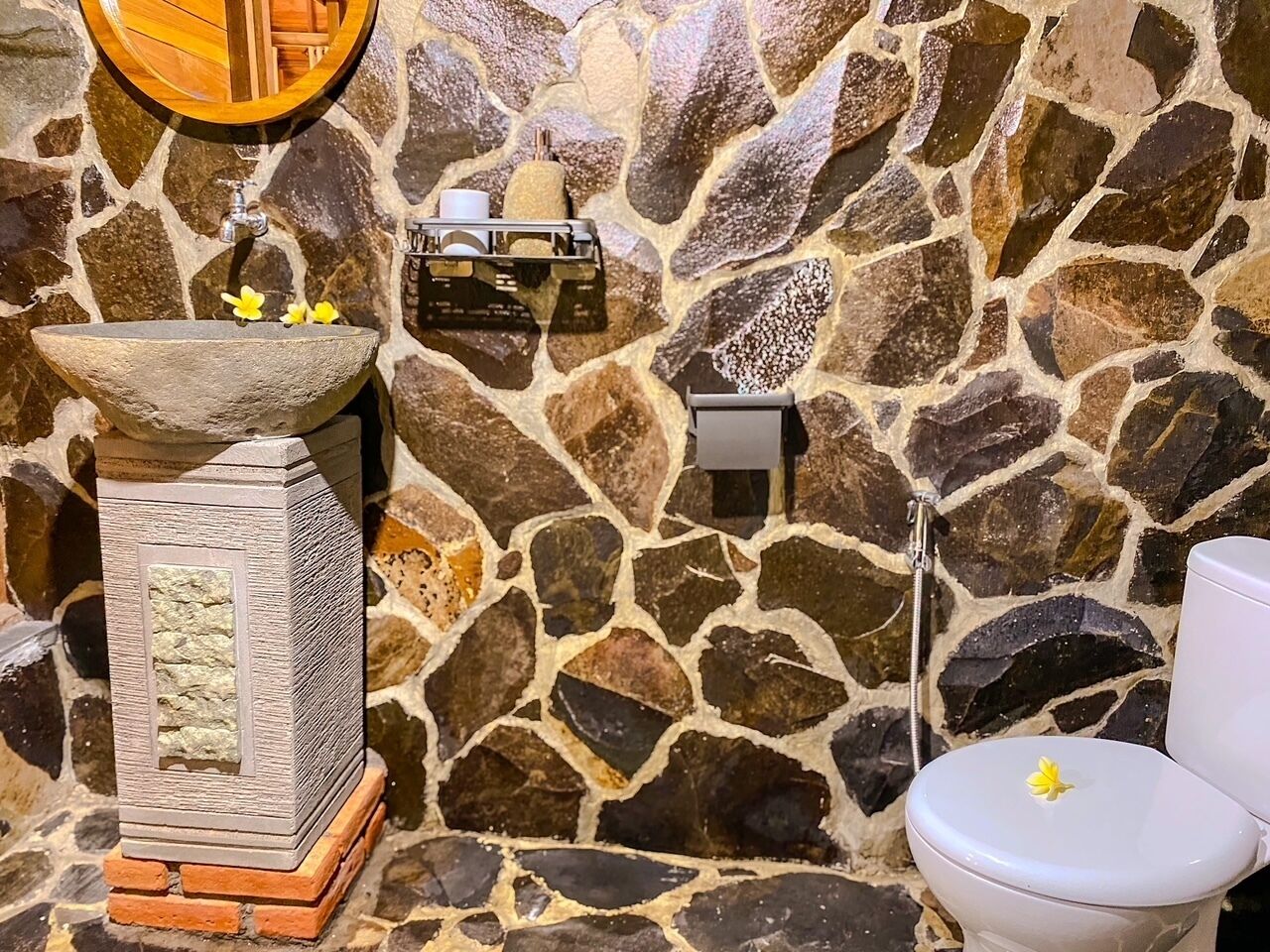 A bathroom with a stone wall, a sink with a wooden basin, a toilet, and a mirror.