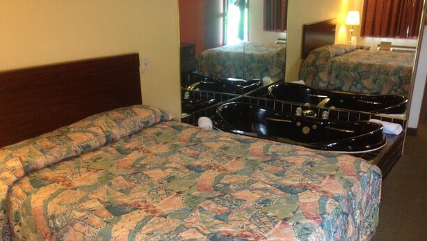 A hotel room with two beds, each with patterned bedding, a large black bathtub, and a mirror reflecting the room. - Guest Inn Lebanon (Lebanon)