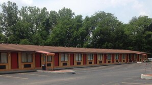 A motel with a row of single-story buildings, a parking lot, and trees in the background. - Guest Inn Lebanon (Lebanon)