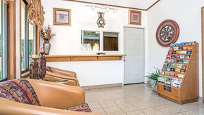 A reception area with a desk, a waiting area with chairs, a wall clock, framed artwork, and a display rack with cards. - Guest Inn Lebanon (Lebanon)